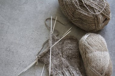 Organik yünden yapılmış sıcak çoraplar ördüm. Kahverengi çorap, örgü iğneleri ve doğal iplik yumağının yakın çekimi. Kopyalama alanı olan gri arkaplan. 