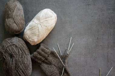 Organik yünden yapılmış sıcak çoraplar ördüm. Kahverengi çorap, örgü iğneleri ve doğal iplik yumağının yakın çekimi. Kopyalama alanı olan gri arkaplan. 