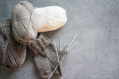 Organik yünden yapılmış sıcak çoraplar ördüm. Kahverengi çorap, örgü iğneleri ve doğal iplik yumağının yakın çekimi. Kopyalama alanı olan gri arkaplan. 