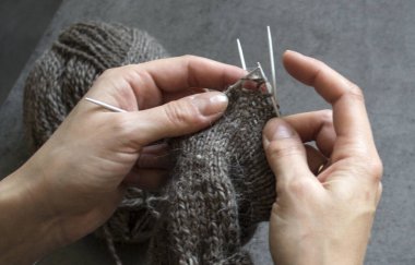 Kadın elleri örgü iğnelerini tutuyor. Gri arkaplanda fotokopi alanı olan bir fotoğrafı kapat. Sıcak çorap örüyorum.. 
