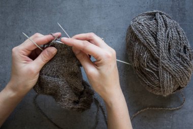 Kadın elleri örgü iğnelerini tutuyor. Gri arkaplanda fotokopi alanı olan bir fotoğrafı kapat. Sıcak çorap örüyorum.. 