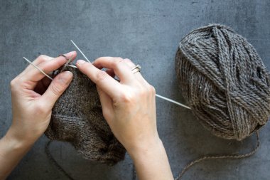 Kadın elleri örgü iğnelerini tutuyor. Gri arkaplanda fotokopi alanı olan bir fotoğrafı kapat. Sıcak çorap örüyorum.. 