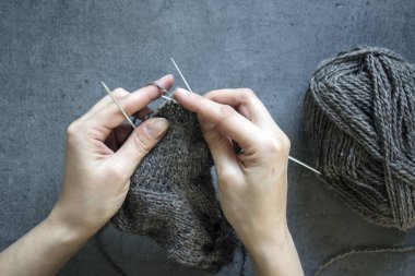 Kadın elleri örgü iğnelerini tutuyor. Gri arkaplanda fotokopi alanı olan bir fotoğrafı kapat. Sıcak çorap örüyorum.. 