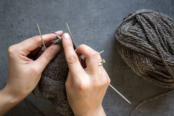 Cozy knitting. Brown wool socks on grey background. Needle work in progress. Natural sheep wool sock close up photo.