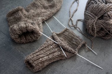 Samimi örgü örüyorum. Gri arka planda kahverengi yün çoraplar. İğne işlemi devam ediyor. Doğal koyun yün çorabı. Yakın çekim fotoğrafı..