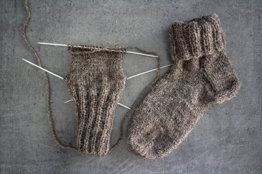 Samimi örgü örüyorum. Gri arka planda kahverengi yün çoraplar. İğne işlemi devam ediyor. Doğal koyun yün çorabı. Yakın çekim fotoğrafı..