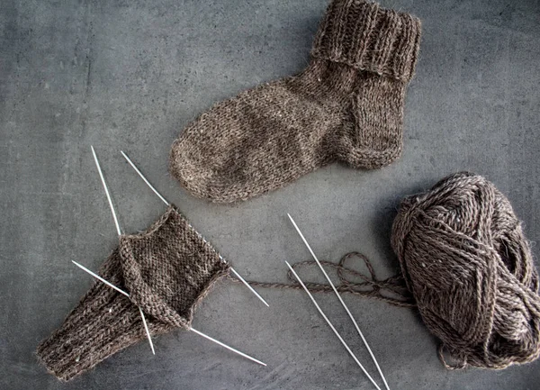 Samimi örgü örüyorum. Gri arka planda kahverengi yün çoraplar. İğne işlemi devam ediyor. Doğal koyun yün çorabı. Yakın çekim fotoğrafı..