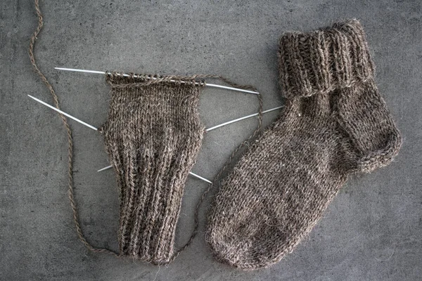 Samimi örgü örüyorum. Gri arka planda kahverengi yün çoraplar. İğne işlemi devam ediyor. Doğal koyun yün çorabı. Yakın çekim fotoğrafı..