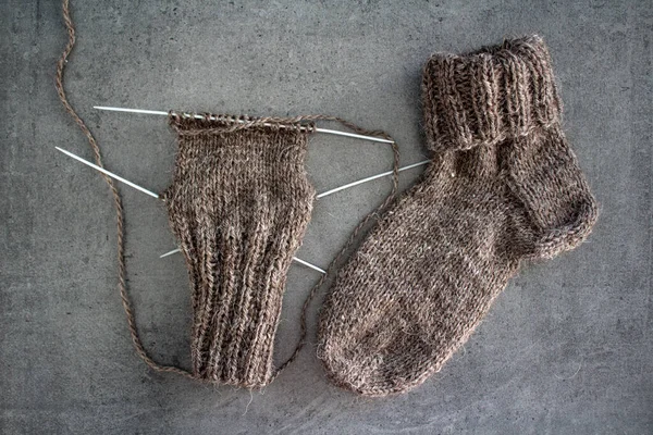 Samimi örgü örüyorum. Gri arka planda kahverengi yün çoraplar. İğne işlemi devam ediyor. Doğal koyun yün çorabı. Yakın çekim fotoğrafı..