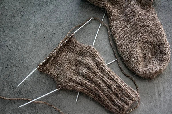Samimi örgü örüyorum. Gri arka planda kahverengi yün çoraplar. İğne işlemi devam ediyor. Doğal koyun yün çorabı. Yakın çekim fotoğrafı..