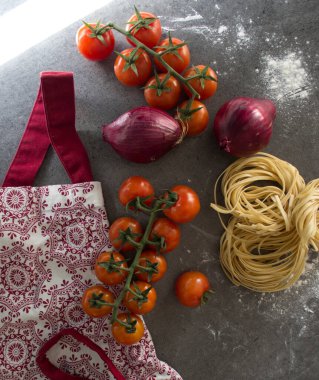 Masadaki makarna malzemeleri. Çiğ spagetti ve tagliatelle makarna, kiraz domatesleri ve arka plandaki gri dokuma üzerinde deniz tuzu fotokopisi. Sağlıklı yeme kavramı.