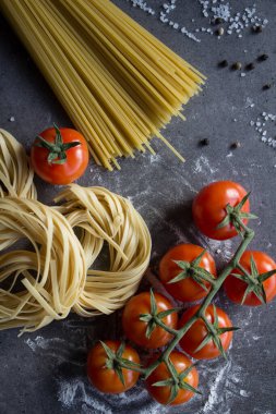 Tagliatelle makarnası, spagetti ve vişneli domatesler gri desenli arka plan. İtalyan yemeği. Üst görüntüdeki taze malzemeler..
