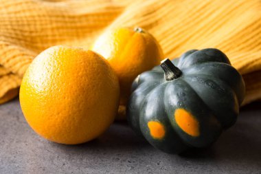 Küçük dekoratif kabak ve masada iki portakal. Sarı arka plan. Taze mevsimlik meyve ve sebzeler. 