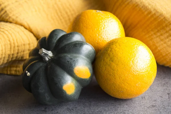 Acorn squash and two oranges on a table. Yellow textured background. Simple composition still life. Healthy eating concept.