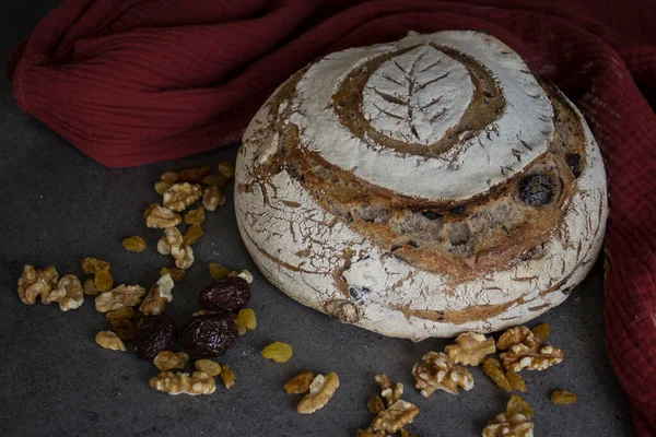 Sourdough bread with a leaf pattern on the top. Whole grain bread with black olives, raisins and nuts. Healthy eating concept. Long-fermented sourdough loaf top view photo. Beautiful round whole grain bread on a table. Still life food.