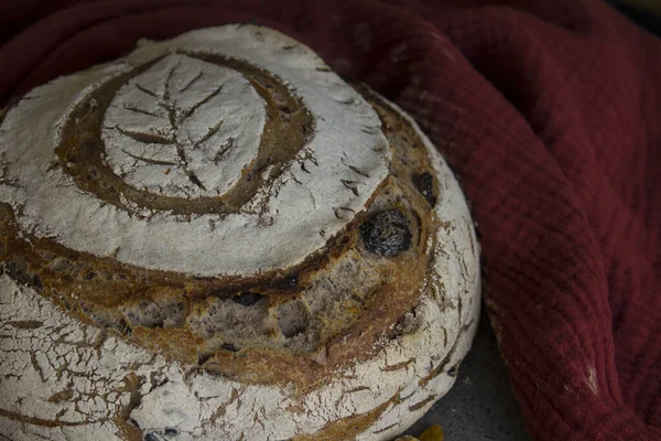 Top view photo of fresh artisan bread made of whole grain flour. Round sourdough bread with leaf pattern on the top. Yellow fabric background. Healthy living concept.