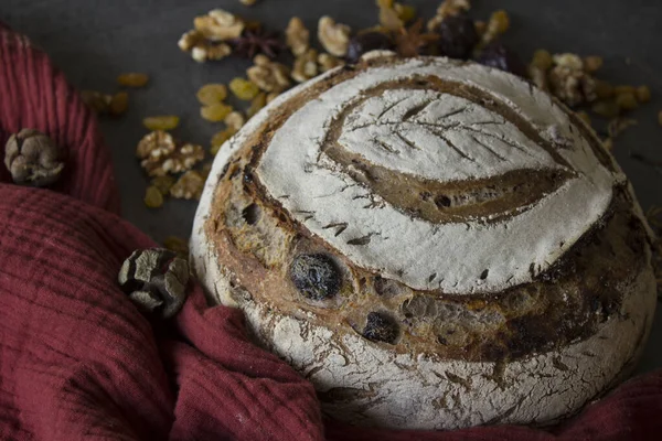 Round sourdough bread with leaf pattern on the top. Yellow fabric background. Healthy living concept. Beautifully scored rye sourdough bread with leaf pattern on the top. Round bread, raisins, green leaves and fruits on yellow fabric background.