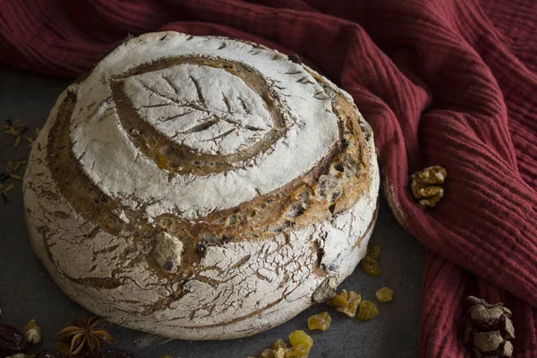 Round sourdough bread with leaf pattern on the top. Yellow fabric background. Healthy living concept. Beautifully scored rye sourdough bread with leaf pattern on the top. Round bread, raisins, green leaves and fruits on yellow fabric background.