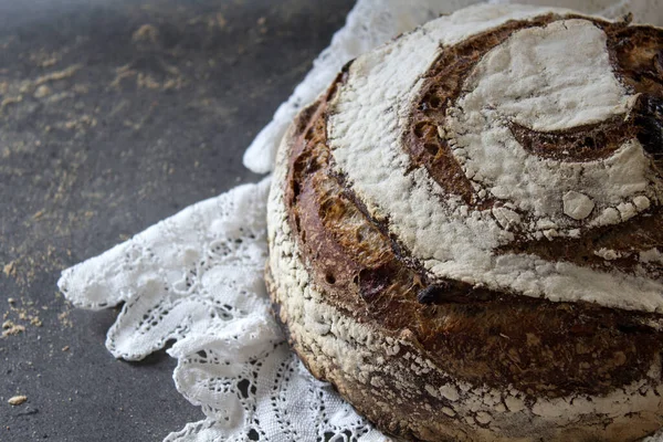 Round rye sourdough bread on white crocheted table cloth. Long-fermented sourdough loaf top view photo. Beautiful round whole grain bread on a table. Still life food.Healthy eating concept.