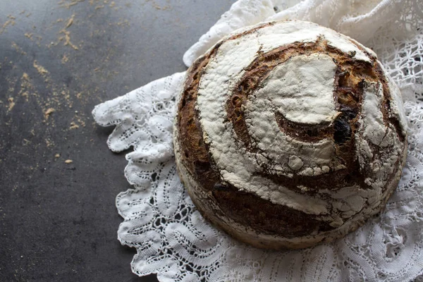 Round rye sourdough bread on white crocheted table cloth. Long-fermented sourdough loaf top view photo. Beautiful round whole grain bread on a table. Still life food.Healthy eating concept.