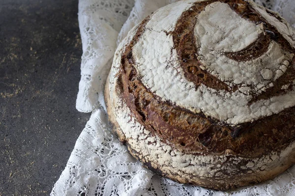 Round rye sourdough bread on white crocheted table cloth. Long-fermented sourdough loaf top view photo. Beautiful round whole grain bread on a table. Still life food.Healthy eating concept.