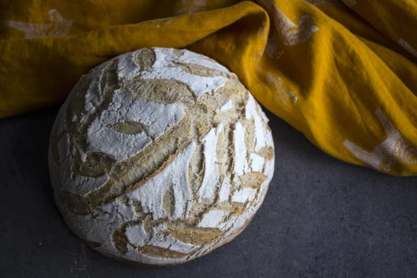 Round sourdough bread on a table. Crusty loaf texture close up. Top view photo of freshly baked artisan bread. Gray textured background. Healthy eating concept.