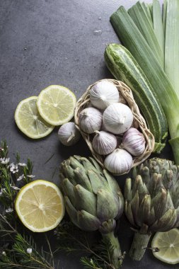 Masada taze enginarlar var. Pişmemiş sebzelerin en iyi görüntüsü: enginar çiçekleri, limon dilimleri, pırasa ve bitkiler. Yine de hayat yemeği. Dengeli diyet kavramı. 