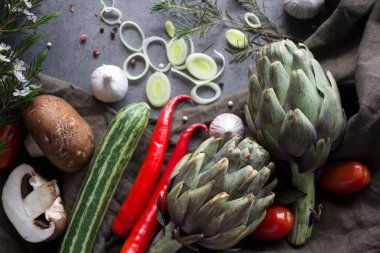 Masadaki taze sebzelerin renkli bir fotoğrafı. Kirazlı domates, enginar, limon dilimleri, pırasa, biber, kabak ve yeşil badem resmi. Gri desenli arka plan. Sağlıklı yeme kavramı. 