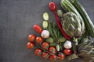 Masadaki taze sebzelerin renkli bir fotoğrafı. Kirazlı domates, enginar, limon dilimleri, pırasa, biber, kabak ve yeşil badem resmi. Gri desenli arka plan. Sağlıklı yeme kavramı. 