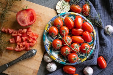 Mavi seramik tabakta doğranmış domates, sarımsak soğanı, otlar ve kiraz domatesleri. Yemek hazırlama fotoğrafı. Taze mevsimlik sebzeler kapanıyor. Sağlıklı yeme kavramı. 