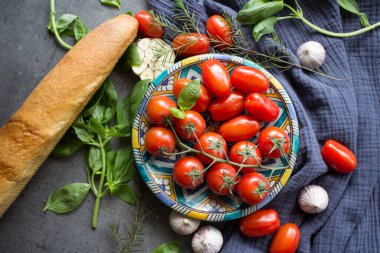 Kiraz domatesleri, fesleğen yaprakları, sarımsak soğanları, bitkiler ve biber. Hughchetta malzemelerinin üst görüntü fotoğrafı. Gri desenli arka plan ve kopyalama alanı. Geleneksel İtalyan yemekleri.