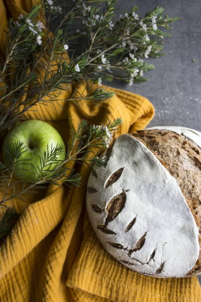 Round sourdough bread decorated with leaf pattern.  Beautiful freshly baked rye bread. Crusty loaf texture close up. Top view photo of homemade bread on yellow kitchen towel.  Dark background with copy space.