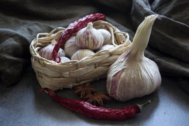 Sarımsaklı hayat. Sepette küçük yuvarlak sarımsak, sarımsak soğanları ve gri desenli arka planda eldivenler.. 