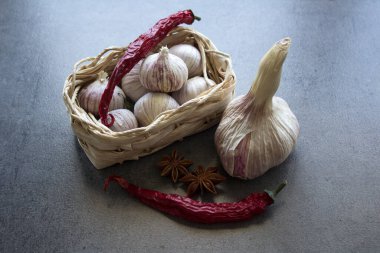 Sarımsaklı hayat. Sepette küçük yuvarlak sarımsak, sarımsak soğanları ve gri desenli arka planda eldivenler.. 