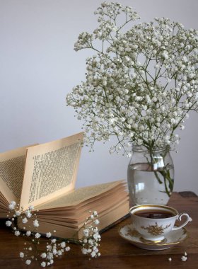 Bir fincan çayla sakin bir hayat. Üzerinde küçük beyaz çiçekler ve bir fincan siyah çay olan basit kompozisyon fotoğrafı. Güzel sabah resmi..