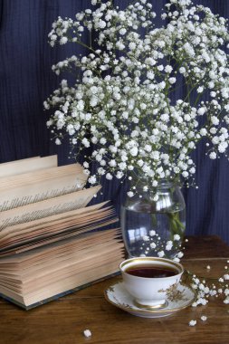 Basit kompozisyon, küçük bir fincan çay, açık kitap ve cam kavanozda çingene çiçekleri ile hayat..  