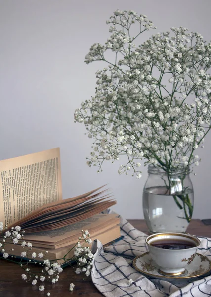 Basit kompozisyon, küçük bir fincan çay, açık kitap ve cam kavanozda çingene çiçekleri ile hayat..  