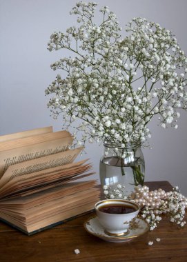 Basit kompozisyon, küçük bir fincan çay, açık kitap ve cam kavanozda çingene çiçekleri ile hayat..  
