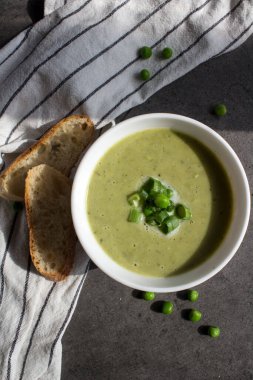 Masada ev yapımı baget ekmek ve kremalı sebze çorbası. Dengeli yeme konsepti. Bir kasedeki yeşil bezelye çorbasını yakından çek. Masa üstü manzaralı yemek. 