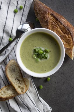 Beyaz kasede yeşil bezelye çorbası, çizgili mutfak havlusunda taze baget ekmeği. Vejetaryen yemeği üst manzara fotoğrafı. Taze konsept yemek.  