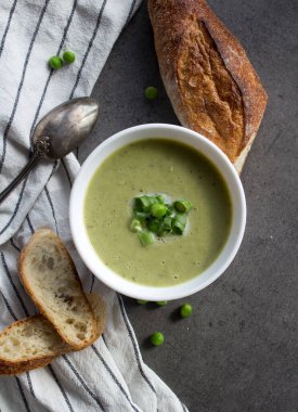 Beyaz kasede yeşil bezelye çorbası, çizgili mutfak havlusunda taze baget ekmeği. Vejetaryen yemeği üst manzara fotoğrafı. Taze konsept yemek.  