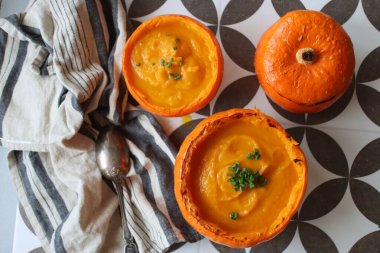 Creamy, nourishing butternut squash soup with a hunk of crusty bread. Fall comfort food. Healthy eating concept. Top view photo of beautiful orange soup served in a squash bowl. 