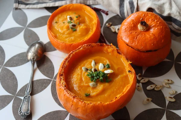 Top view photo of butternut soup in squash bowl. Tasty autumn food on a table. Healthy eating concept. Vegetarian meal recipe. Butternut squash soup served in a squash shell. Creamy fall soup with butternut and carrots in pumpkin bowl.