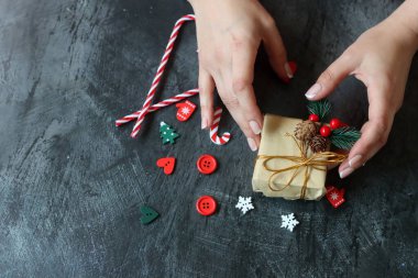 Güzel manikürlü kadın elleri koyu arkaplanda Noel hediyesi taşıyor.