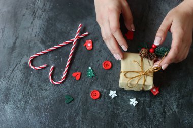 Güzel manikürlü kadın elleri koyu arkaplanda Noel hediyesi taşıyor.