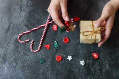 Hediye paketleyen kadın ellerinin yakın çekimi. Koyu gri arkaplan ve metin için boşluk. Noel kutlaması kavramı