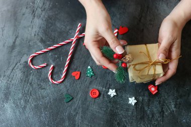 Güzel manikürlü kadın elleri koyu arkaplanda Noel hediyesi taşıyor.