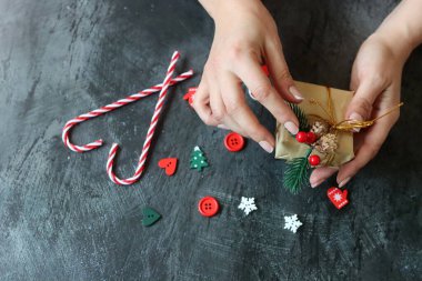 Hediye paketleyen kadın ellerinin yakın çekimi. Koyu gri arkaplan ve metin için boşluk. Noel kutlaması kavramı