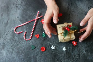 Hediye paketleyen kadın ellerinin yakın çekimi. Koyu gri arkaplan ve metin için boşluk. Noel kutlaması kavramı