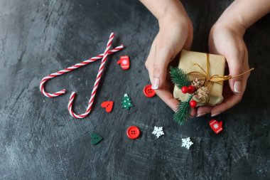 Güzel manikürlü kadın elleri koyu arkaplanda Noel hediyesi taşıyor.